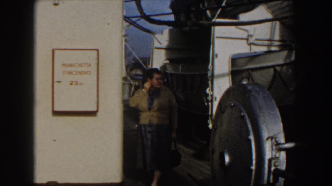 Woman stands near ship machinery and a white wall sign on a bright deck.