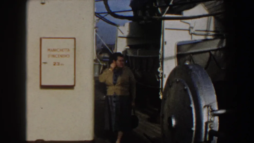 The woman remains on the Gibraltar ship deck, framed by a white fire-hose sign, dark rigging, and a large metal hatch.