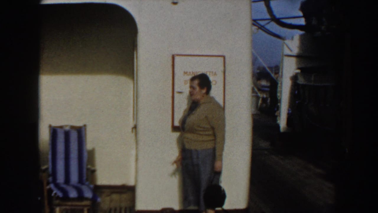 Woman on ship deck facing a man near a wall sign and deck equipment.