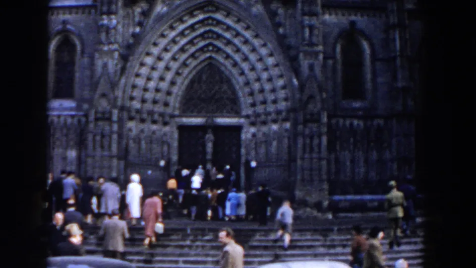 Crowds in mid-century dress move around the steps of a large Gothic-style church in Gibraltar, filmed from a home-movie viewpoint.