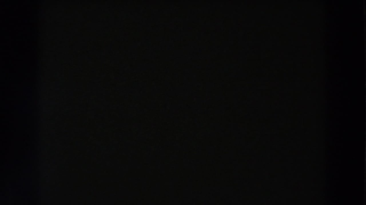 Mostly black 8mm frame with only faint texture visible before the shop scene appears.
