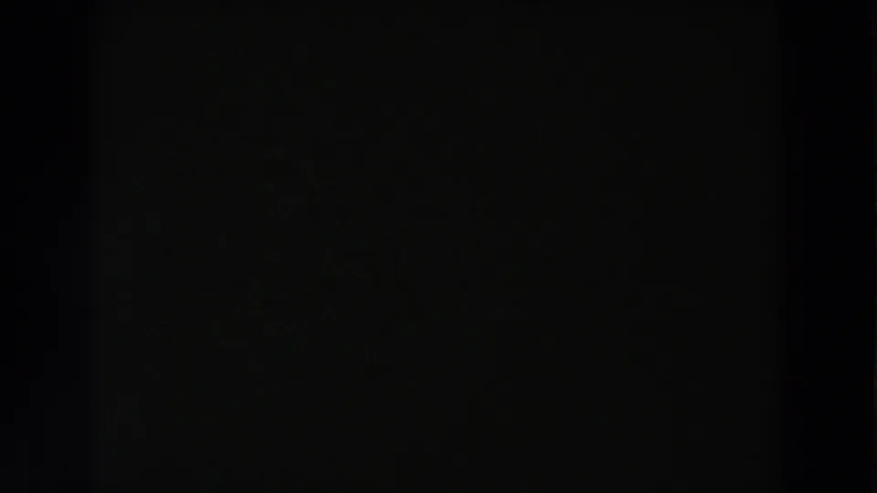 Mostly black 8mm frame with only faint texture visible before the shop scene appears.
