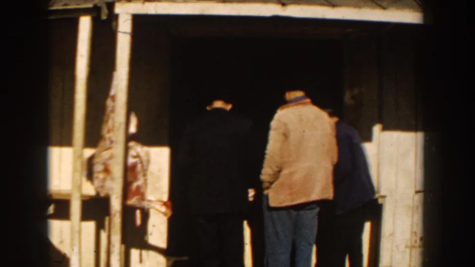 In 1959 Casablanca, three adult men stand near a shaded shop entrance with a hanging meat display at the left.