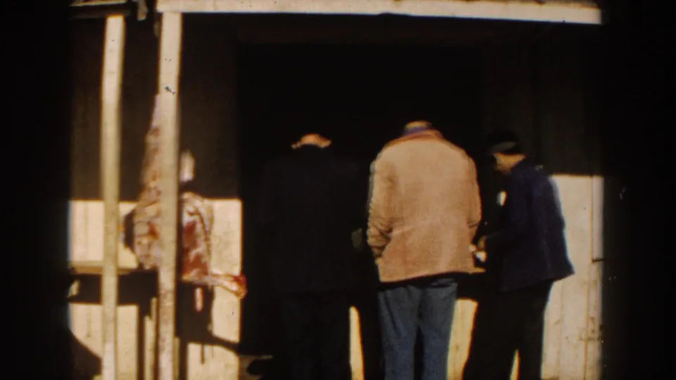 In 1959 Casablanca, adult men pause at a small shop doorway beside a visible hanging meat display.