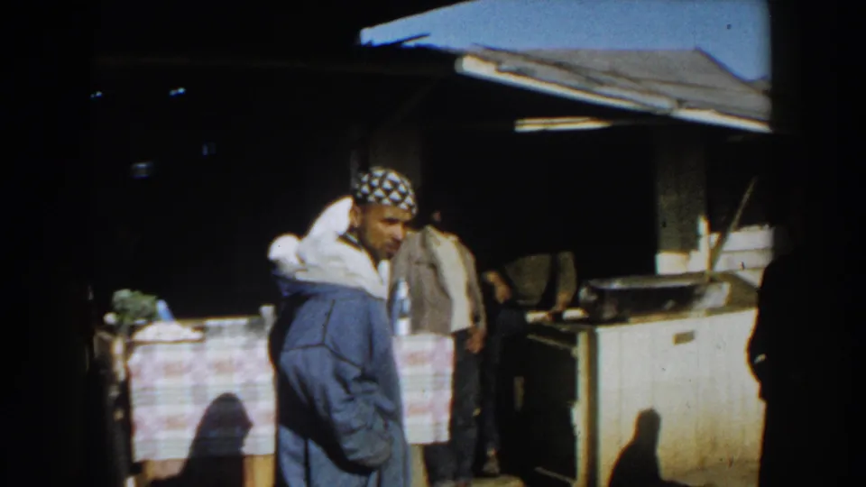 Casablanca 1959 market frame showing a man in a patterned cap beside a covered stall table, with other figures nearby.