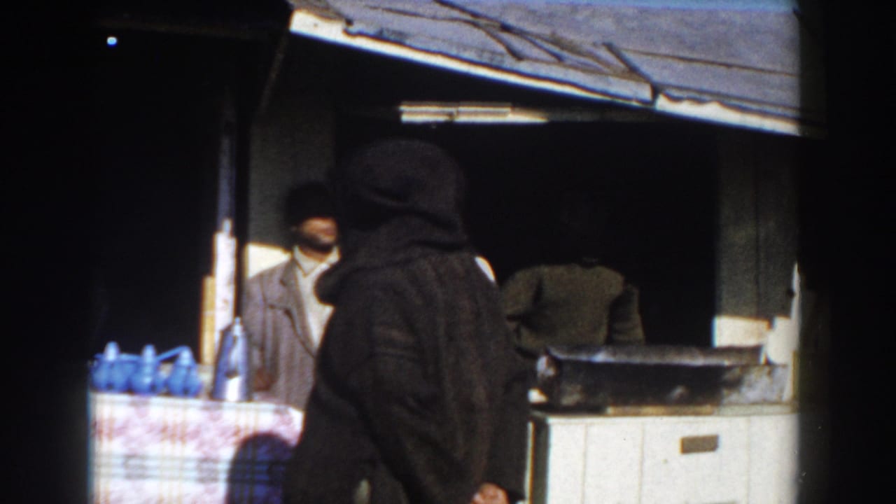 Men stand at a small market stall under a corrugated roof with blue jugs on the counter.