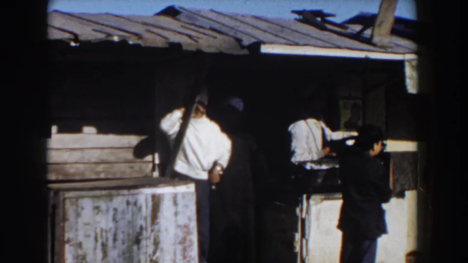 1959 Casablanca home-movie frame looking toward the back of men at a worn food stall under a corrugated awning.