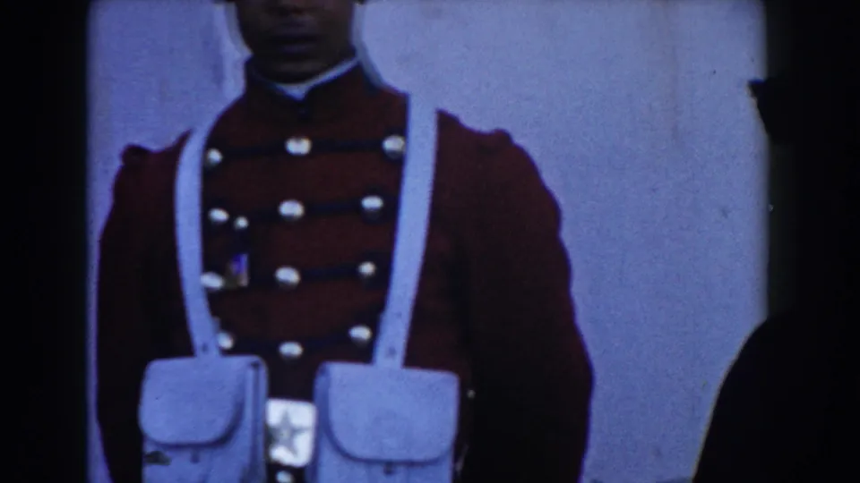 A cropped 1959 Casablanca home-movie frame shows a red-uniformed guard or soldier with white straps standing near a pale wall.