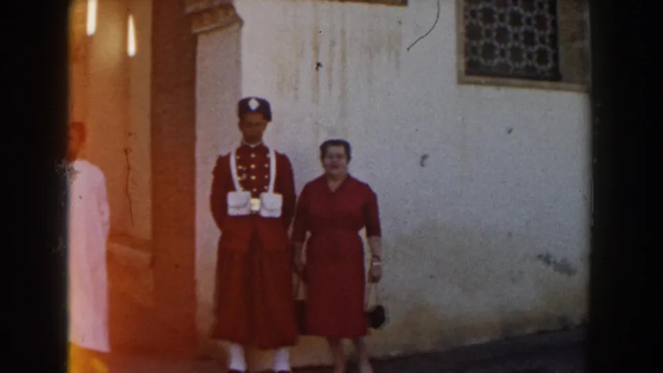 The posed pair remains near the wall while a man in a white robe and red cap passes through the Casablanca street scene.