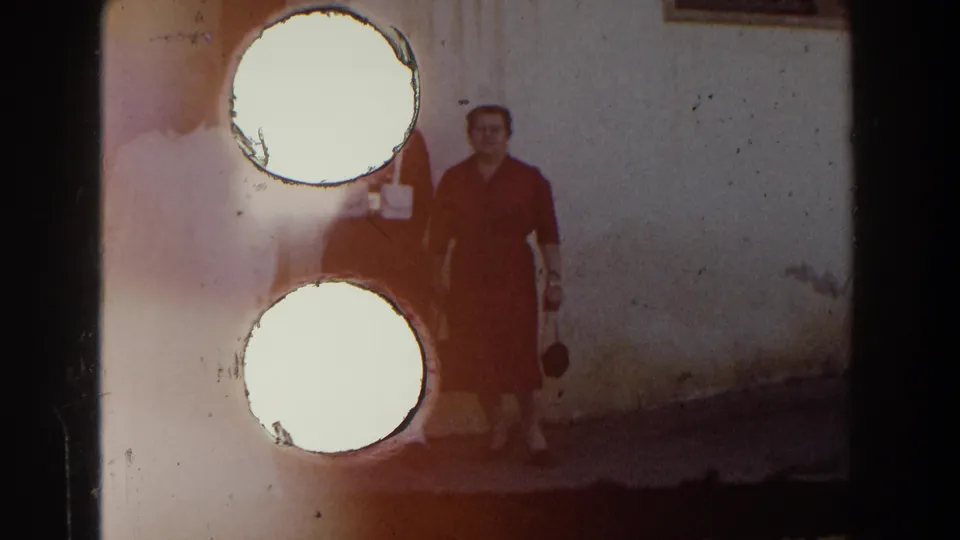 The woman in red remains visible beside the stucco wall while large circular exposure artifacts obscure much of the uniformed man and passing figure.