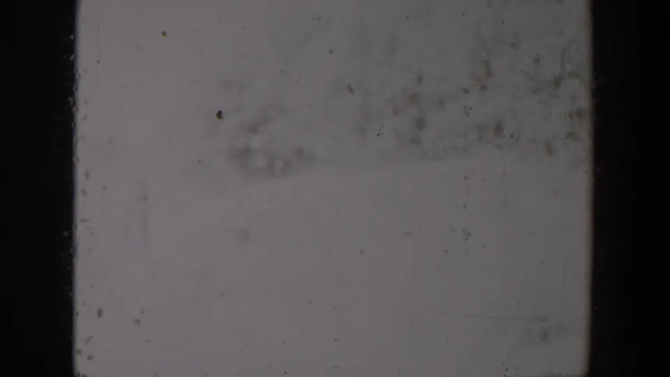 1957 Lubbock-area 8mm frame with a washed snowy field, faint grasses, and a barely defined shrub form.