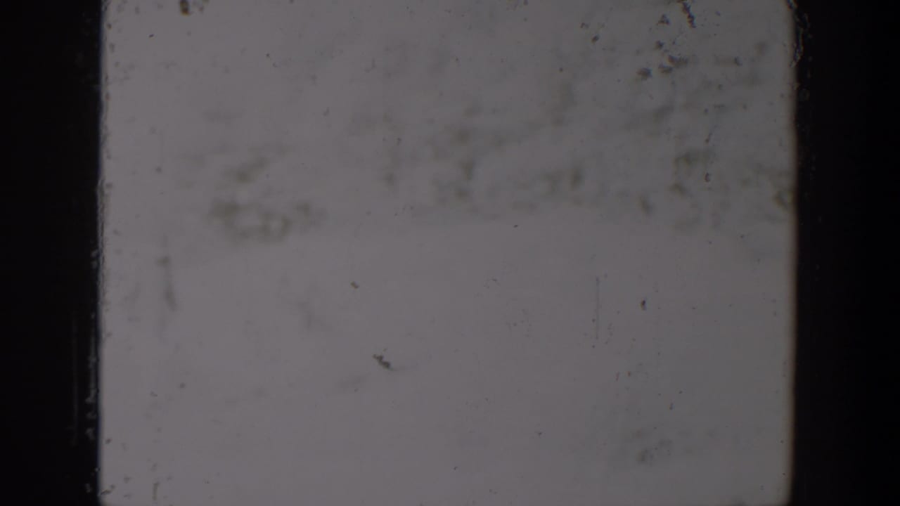 1957 Lubbock-attributed 8mm frame showing a washed gray field, dark film edges, dust specks, scratches, and surface wear.