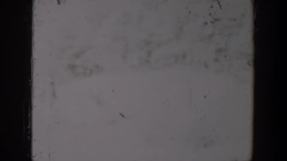 1957 Lubbock-attributed 8mm frame showing a washed gray field, dark film edges, dust specks, scratches, and surface wear.