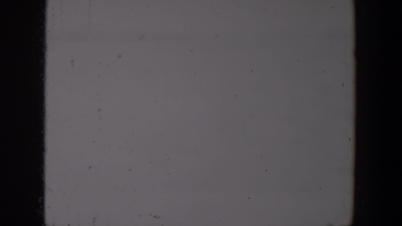 1957 Lubbock 8mm source frame showing a mostly blank gray field with dark film-edge bands, surface dust, scratches, and muted exposure.