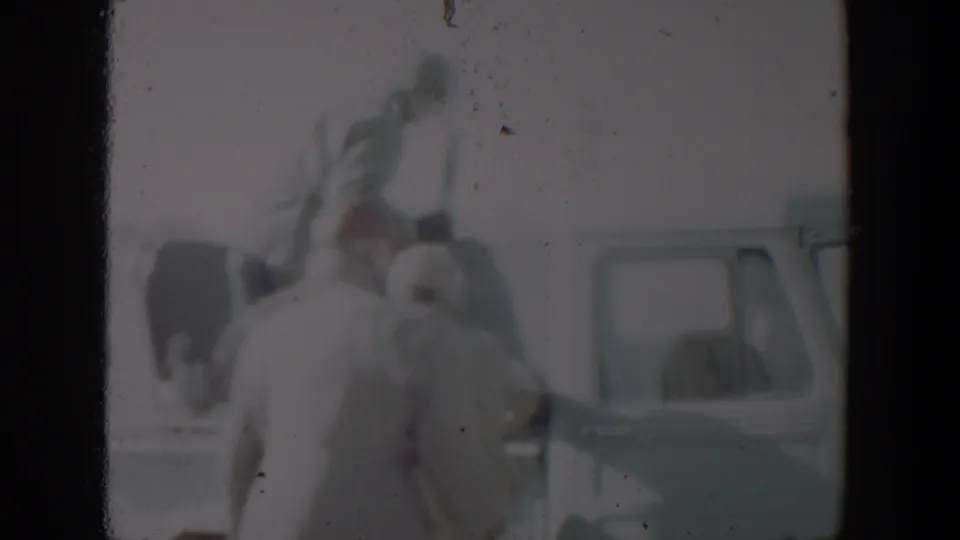 In the supplied 1957 Lubbock footage, adults in coats gather near the side of a pale pickup truck in bright outdoor light.