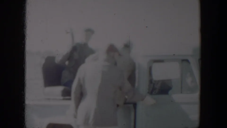 Adults in winter clothing appear around a pale pickup truck in the 1957 Lubbock home-movie scene.