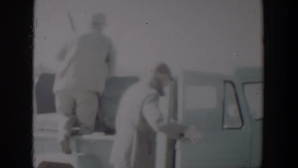 A man steps into the bed of a light-colored pickup as another adult stands near the open cab door in the 1957 Texas home-movie scene.