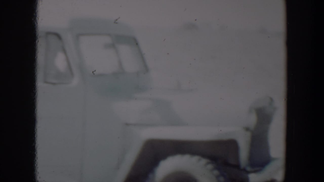 A partial light-colored car appears at the left edge of a soft 1957 8mm frame, likely from the Lubbock, Texas footage.