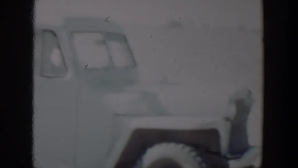 A partial light-colored car appears at the left edge of a soft 1957 8mm frame, likely from the Lubbock, Texas footage.