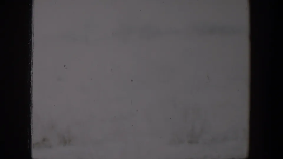 1957 Lubbock home-movie frame showing an indistinct overexposed outdoor surface with faint grass and dust specks.