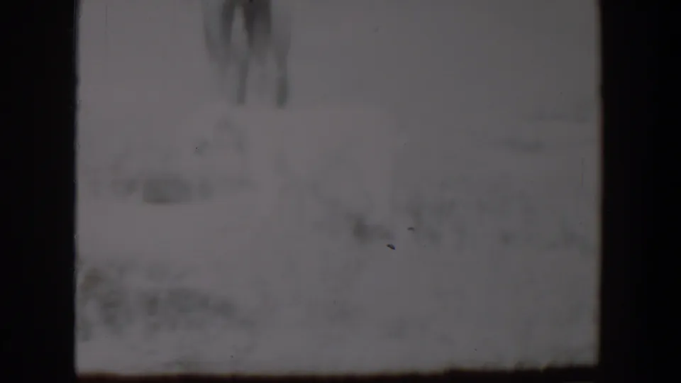 1957 8mm Lubbock snow scene with a pale dog shape and indistinct standing figure partly obscured by grain and exposure.