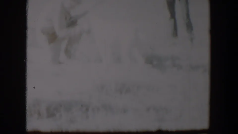 A soft, grainy 1957 Lubbock winter frame shows indistinct dog-and-person activity in snow, partly lost in exposure.