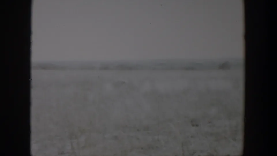 1957 Lubbock, Texas home-movie frame showing a blurred open field through dark vertical borders beneath an overcast sky.