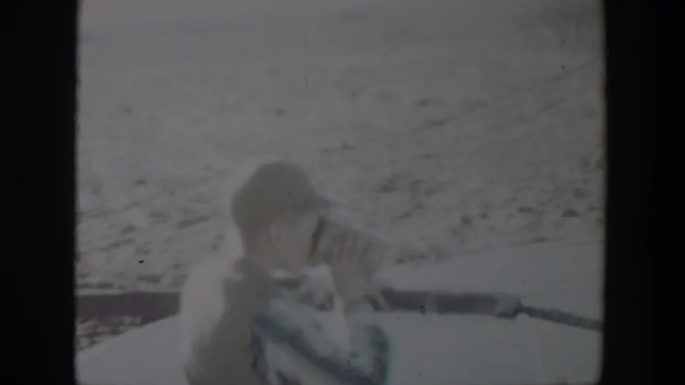 Young boy in a cap drinks from a pipe in a soft 1957 Lubbock home-movie frame.