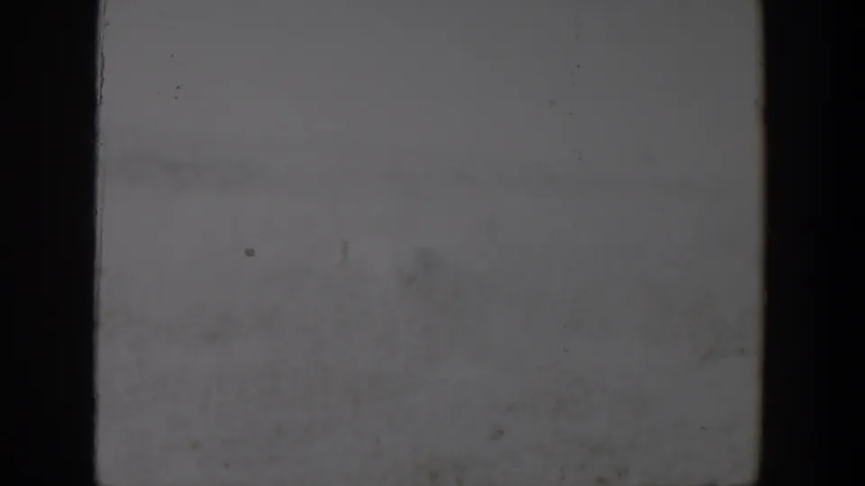 A pale, soft 8mm frame from the 1957 Lubbock, Texas footage shows film gate edges, faint marks, and little visible subject detail.