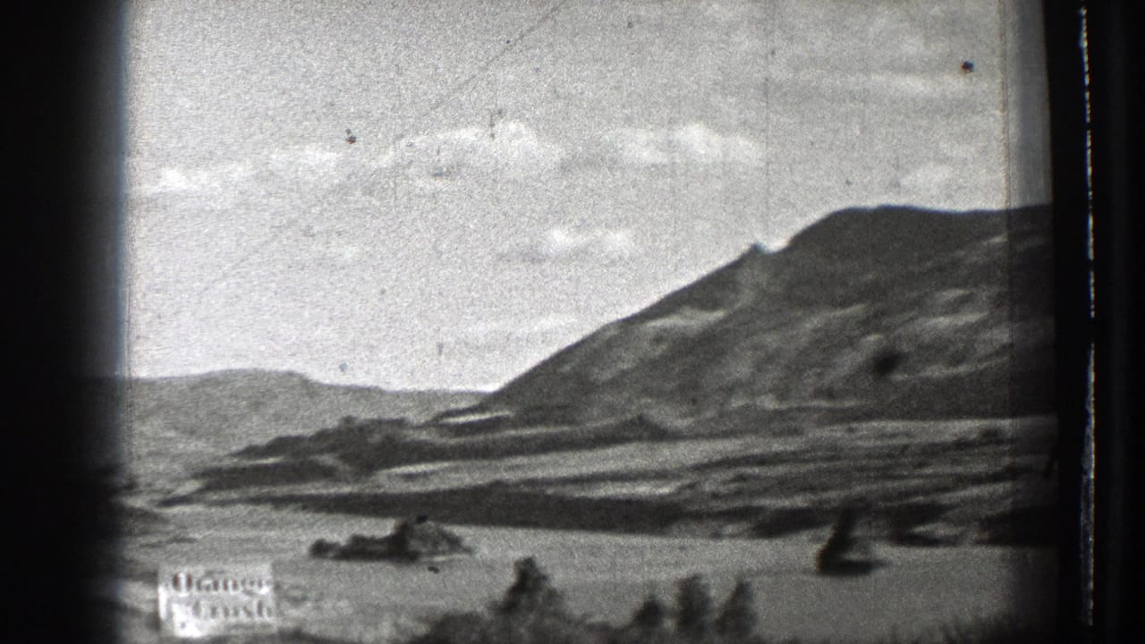 Black-and-white mountain landscape with rocky shoreline or basin and dark film edges.