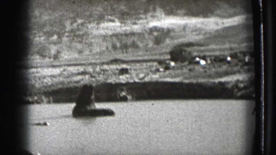 1939 Washington 8mm frame showing a lake, distant hills, shoreline structures, and dark foreground shapes from a moving viewpoint.