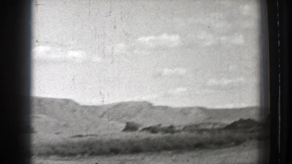 Black-and-white Washington travel frame with low hills, cloudy sky, and a blurred foreground suggesting the camera is moving.