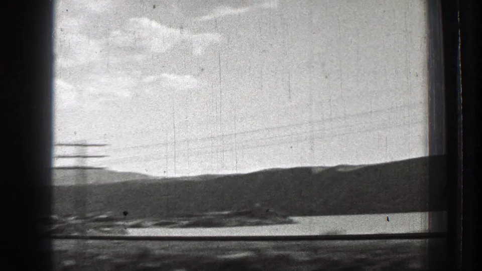 1939 Washington 8mm frame showing a lake, dark hillside, cloudy sky, and passing utility lines from a moving vehicle viewpoint.