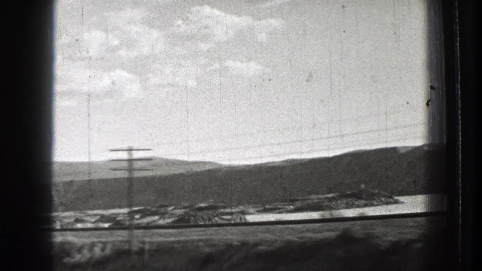 Black-and-white 1939 Washington frame with a utility pole, wires, lakeshore structures, water, hills, and cloudy sky.