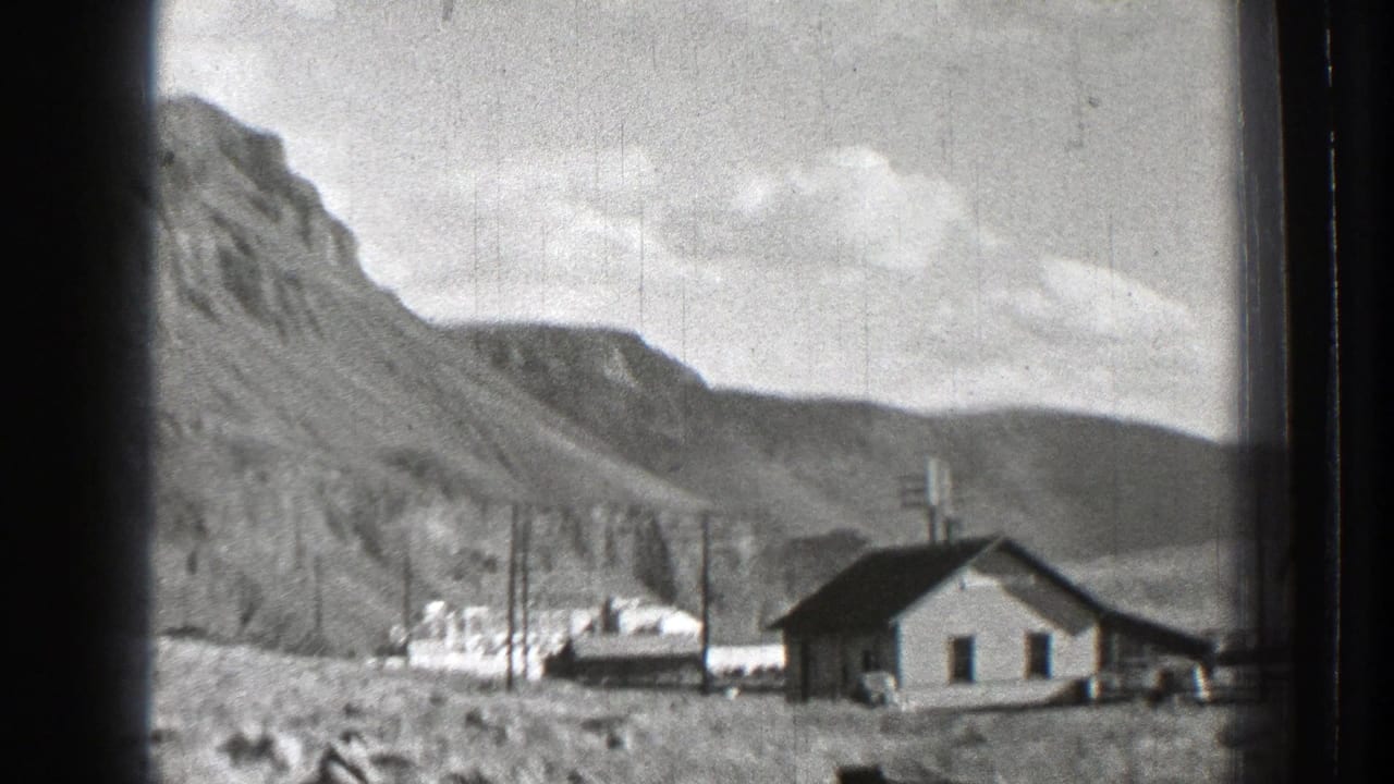 Small roadside house below rocky mountains with utility poles and open sky.