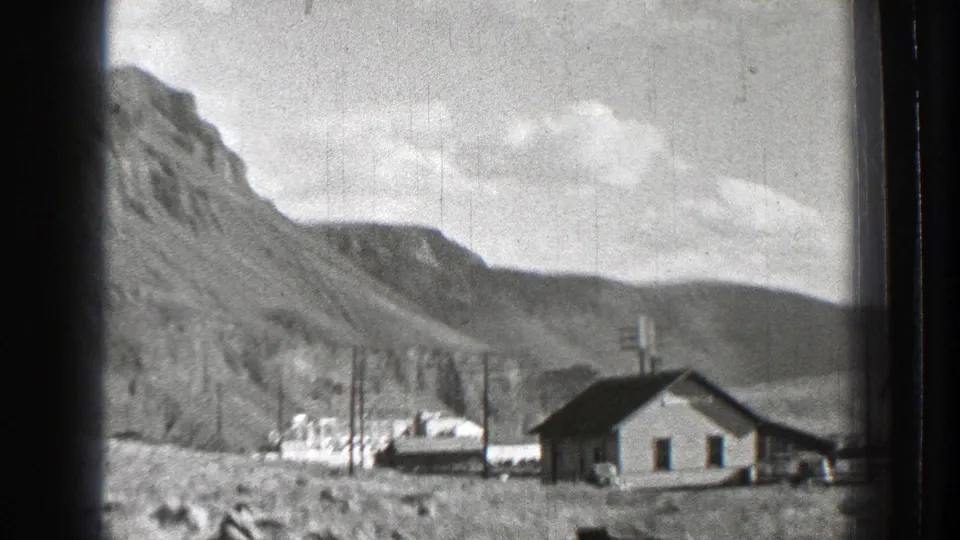 1939 Washington home-movie frame showing a small house near utility poles at the base of steep rocky mountains.