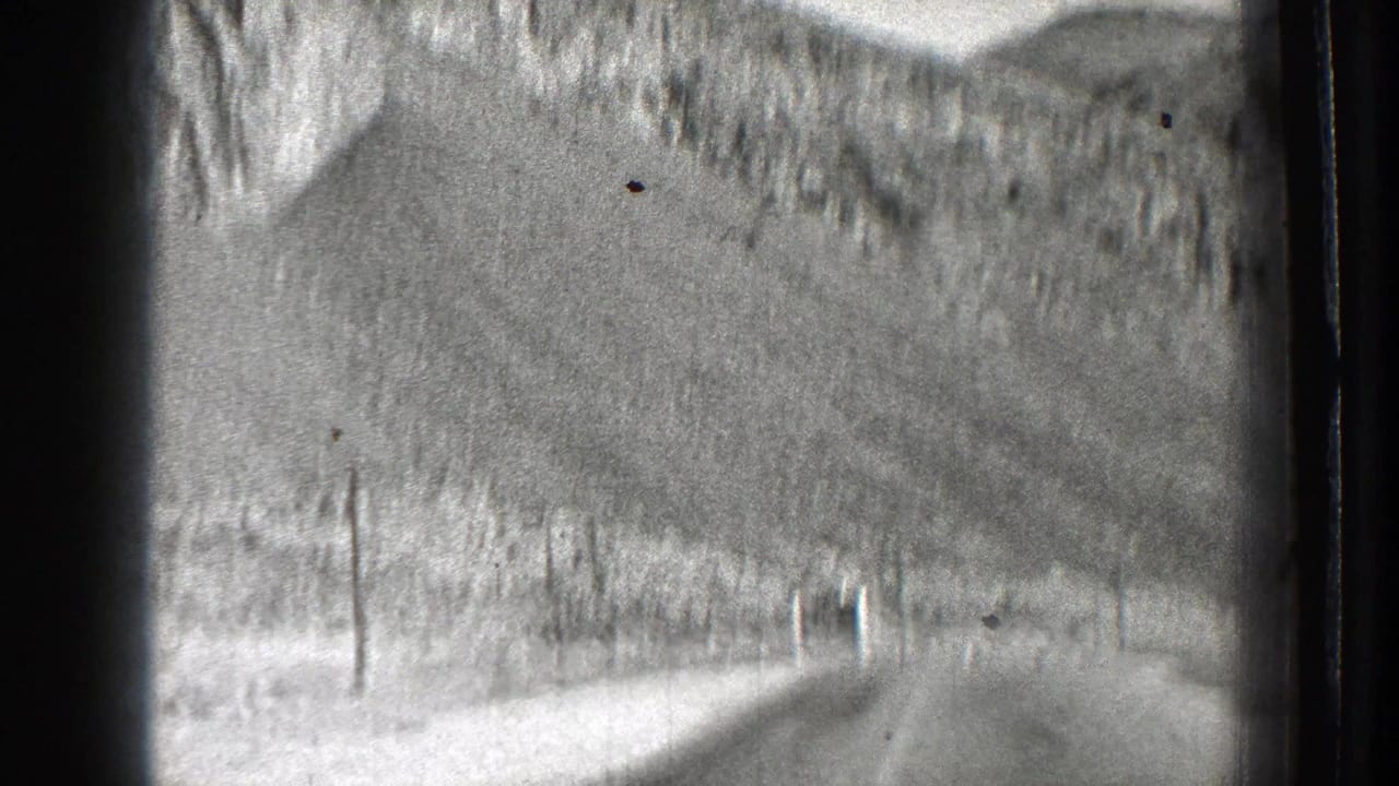 Curving mountain road beside pale rocky slopes and utility poles.