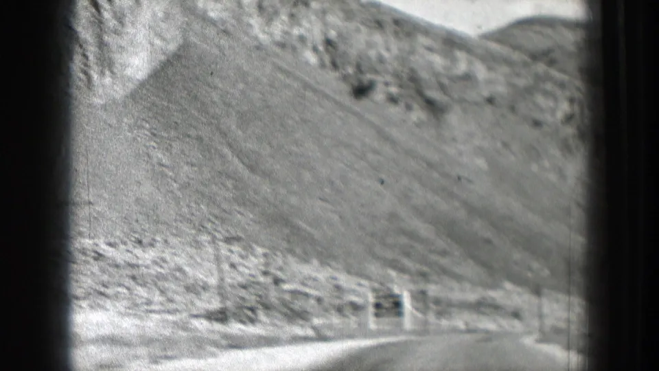 Late-frame Washington road view with a pale rocky hillside, roadside edge, and blurred 8mm home-movie texture.