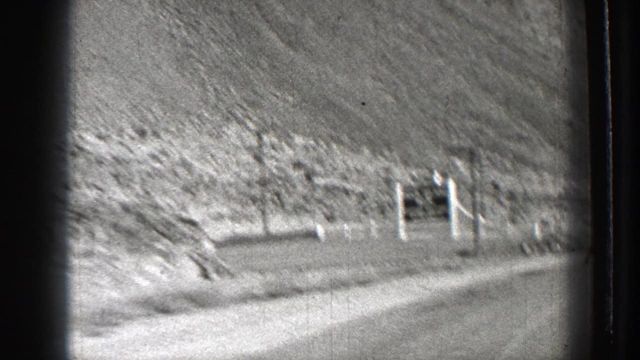 1939 Washington road-trip frame showing a dirt road, arid hillside, and small roadside sign structure viewed from a moving home-movie camera.
