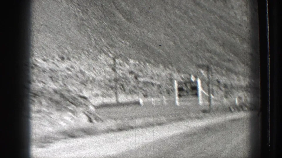 1939 Washington road-trip frame showing a dirt road, arid hillside, and small roadside sign structure viewed from a moving home-movie camera.