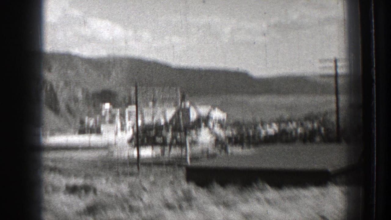 Distant industrial or dam complex with utility poles, fencing, hills, and water or open valley beyond.