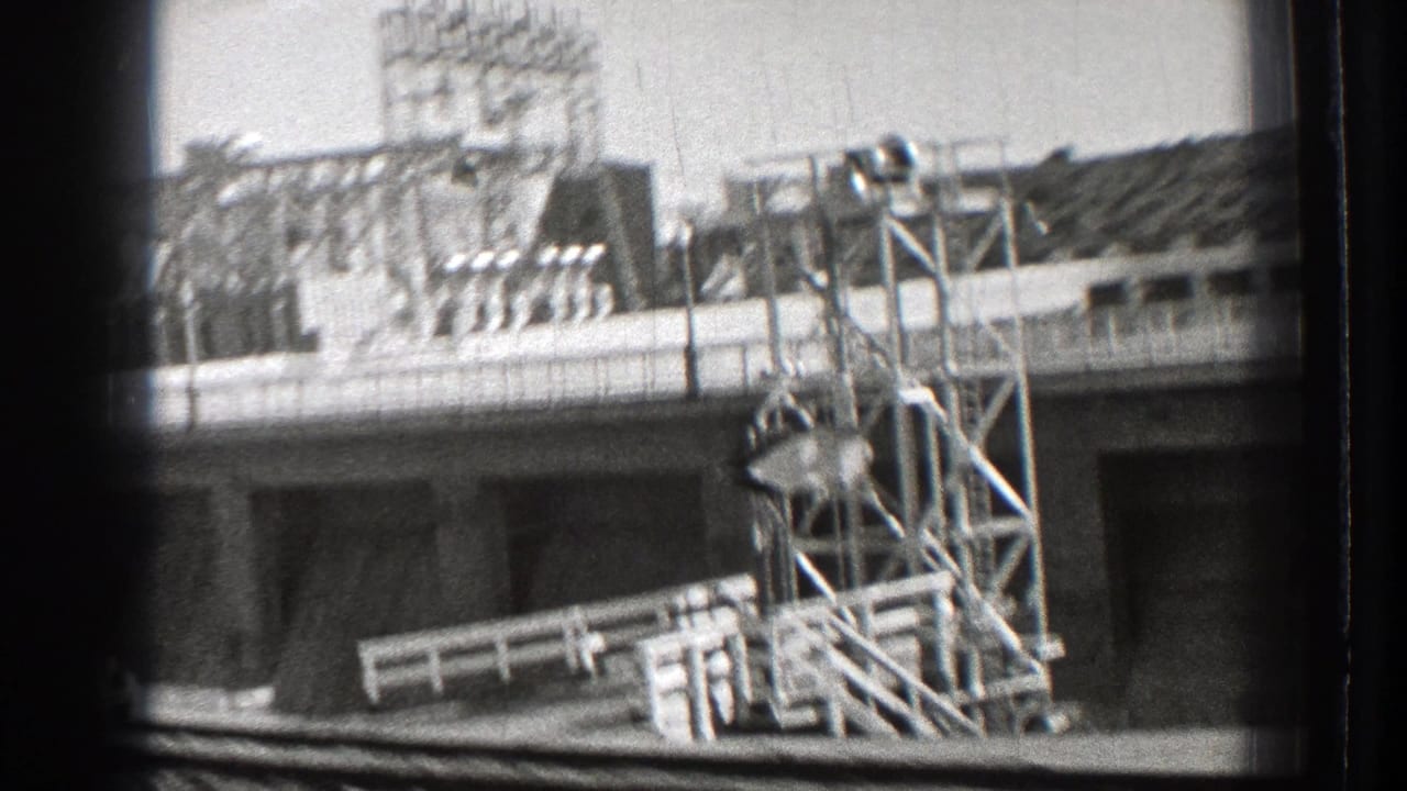 Moving view past a large building with rooftop metal framework and foreground roadway edge.