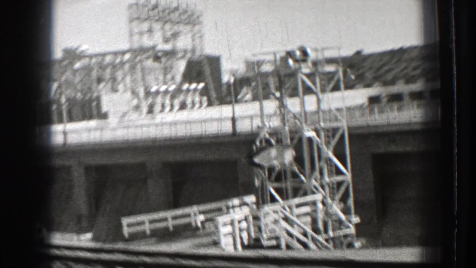 1939 Washington home-movie frame showing a large masonry structure with rooftop framework seen from a moving vehicle.