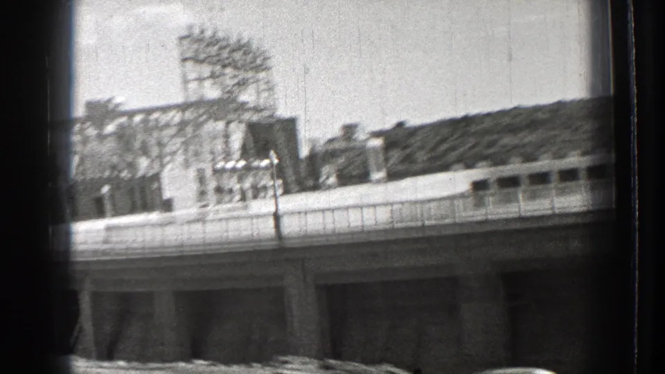 Black-and-white 8mm frame from Washington showing a large structure with railings and rooftop metal framework.