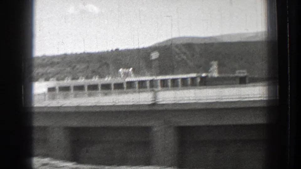 1939 Washington travel frame showing a low roofline, distant hill, and roadside structure in black-and-white 8mm.