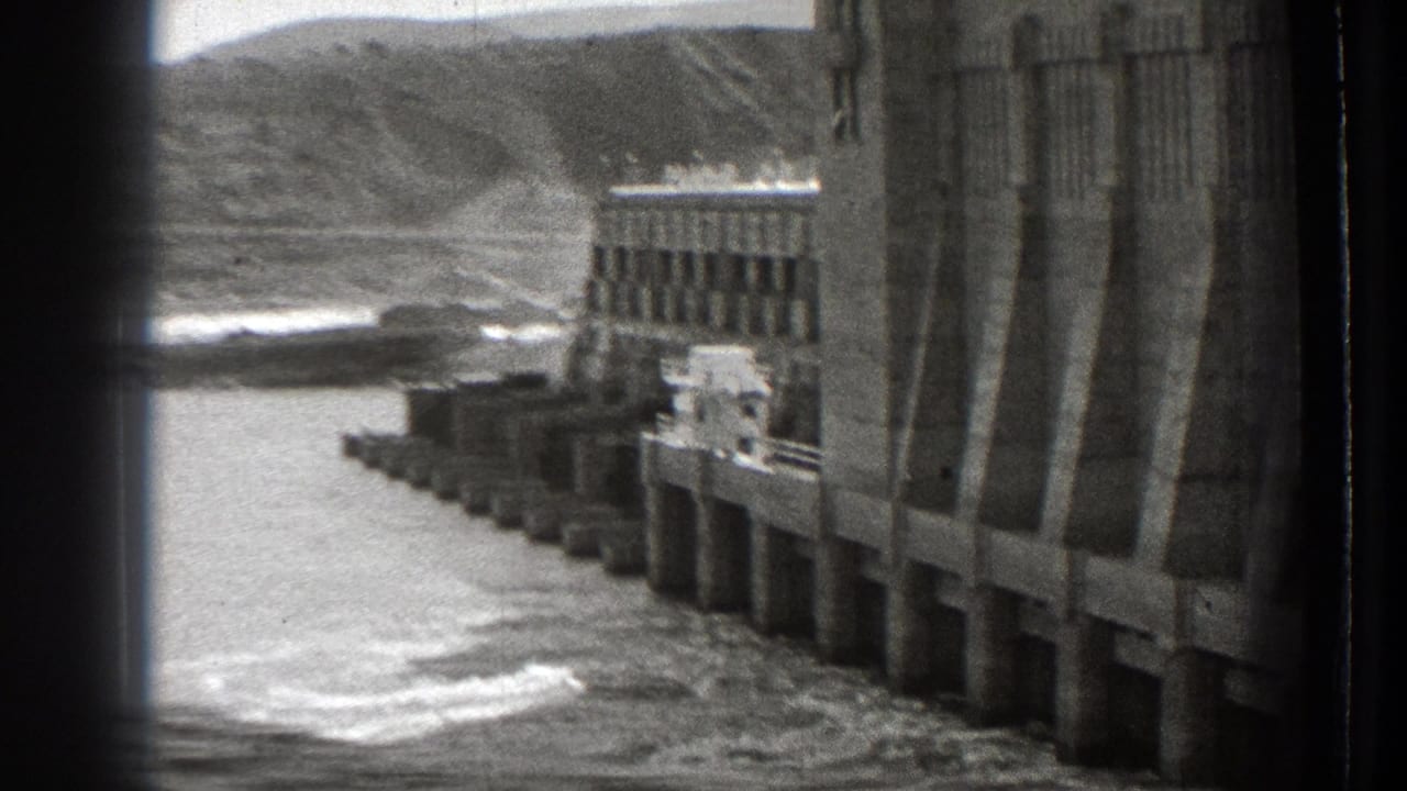 1939 Washington home-movie view of a concrete Columbia River dam, river water, shoreline, and distant hills.