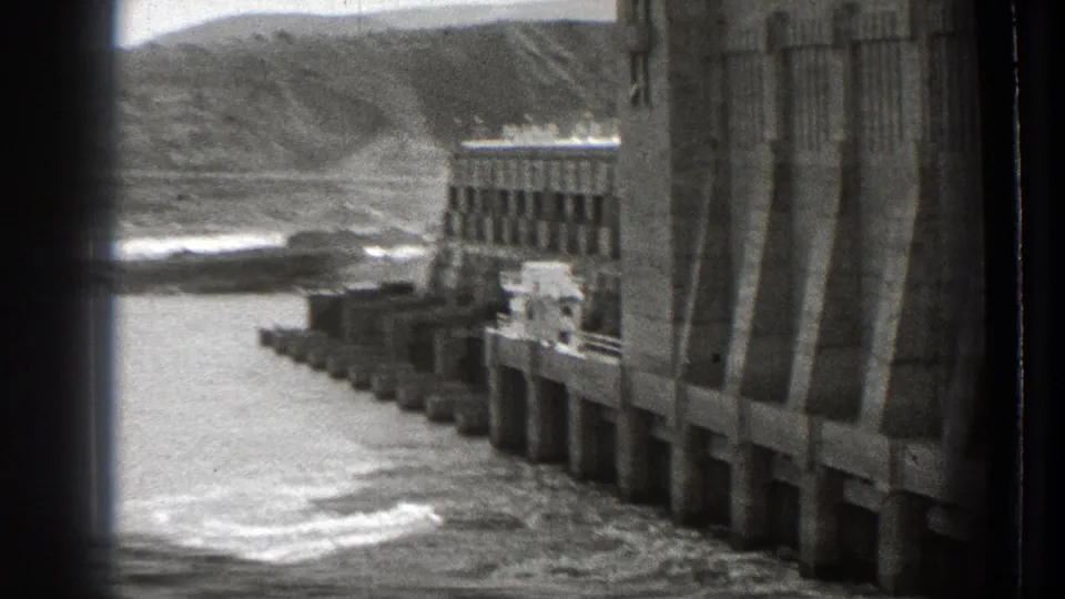 1939 Washington home-movie view of a concrete Columbia River dam, river water, shoreline, and distant hills.
