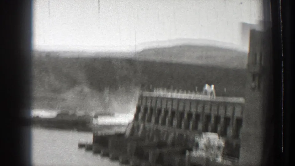 Concrete dam and river spray in a hilly Washington landscape, with small figures visible on the dam crest.