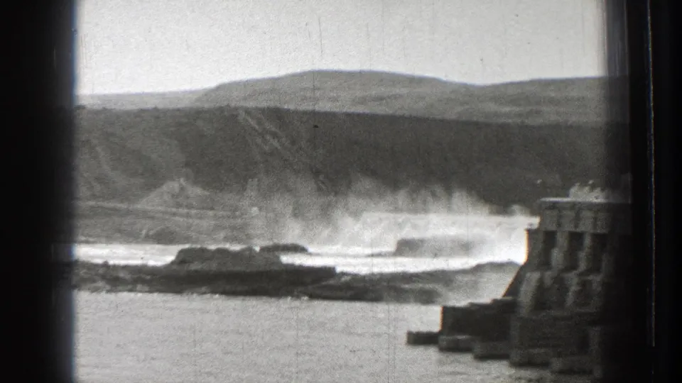 Wide 1939 Washington view of river spray and rocky shoreline beside the edge of a concrete Columbia River dam.