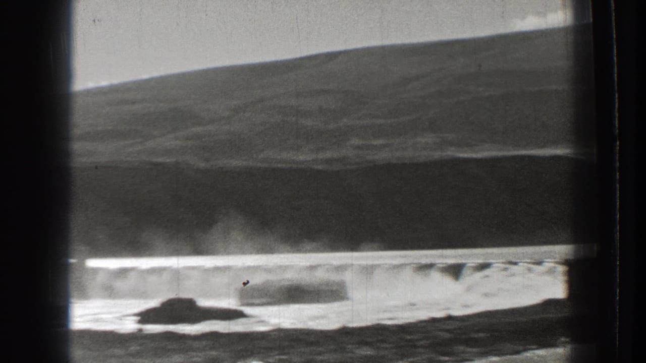 Water cascades across a dam with a dark hill and rock in the foreground.